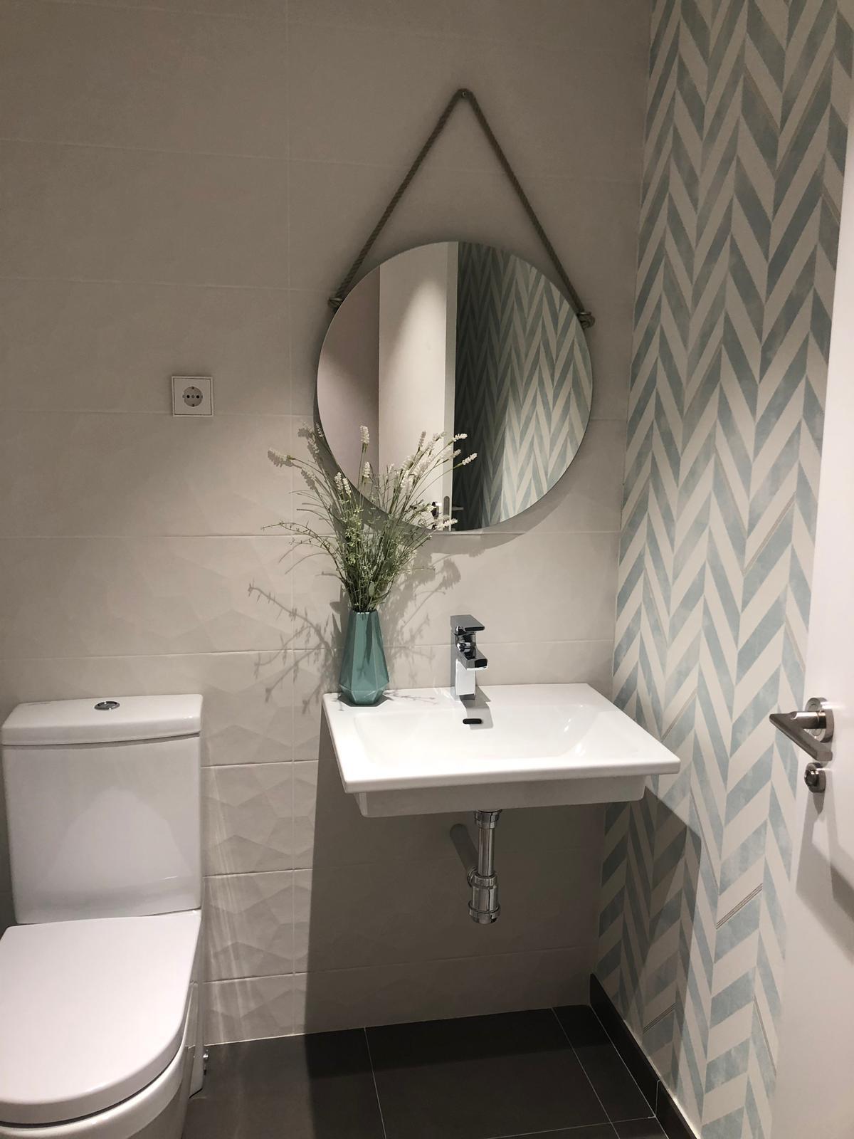 Baño con espejo circular, jarrón de flores secas y azulejo geométrico